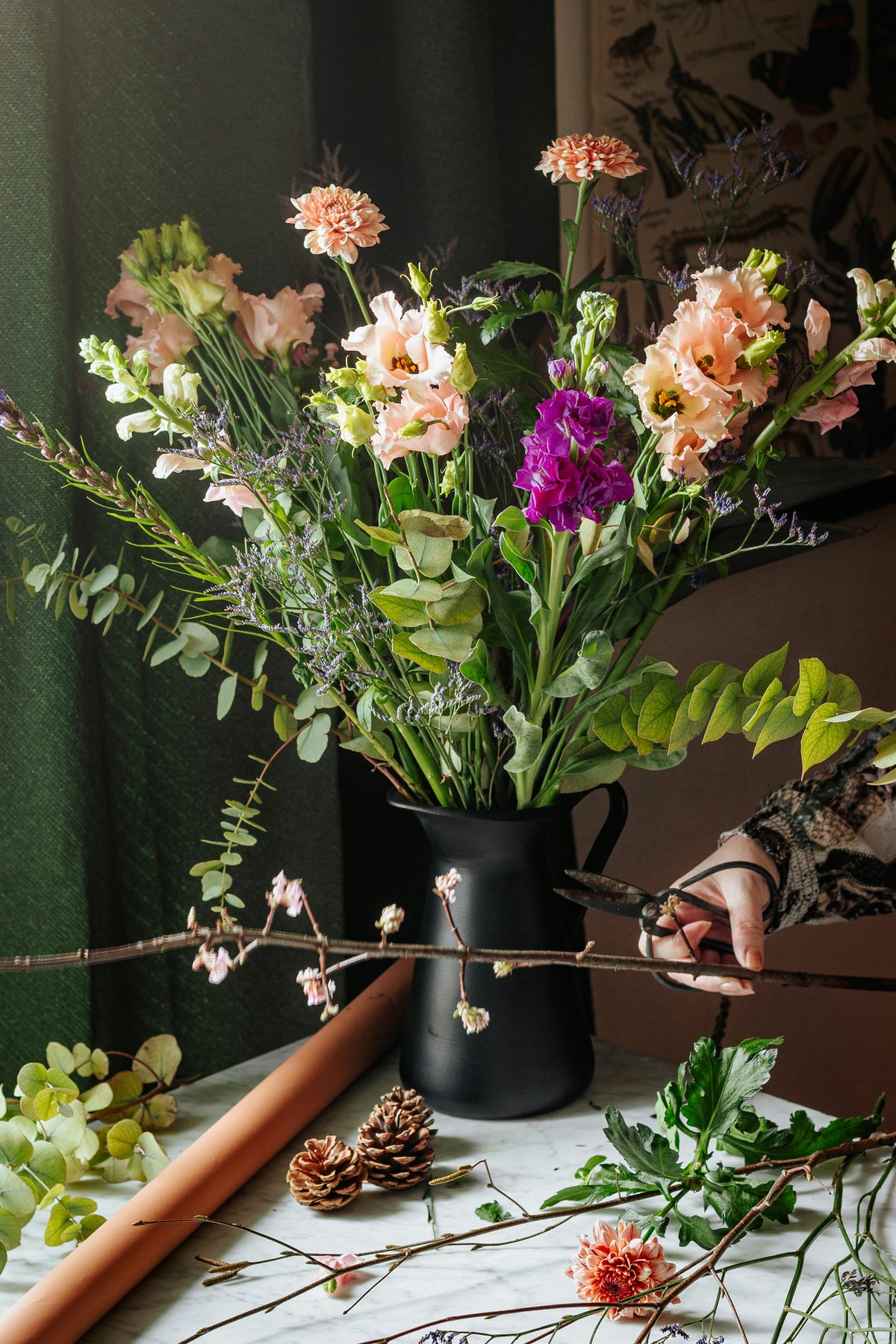 Seasonal stems arranged in a dark pitcher on a work table