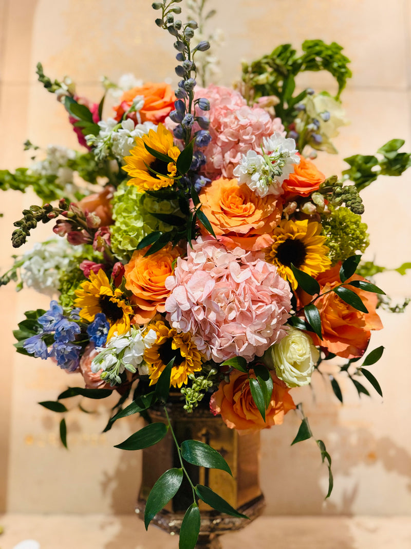 Tall arrangement of roses, sunflowers and hydrangea in a gold urn