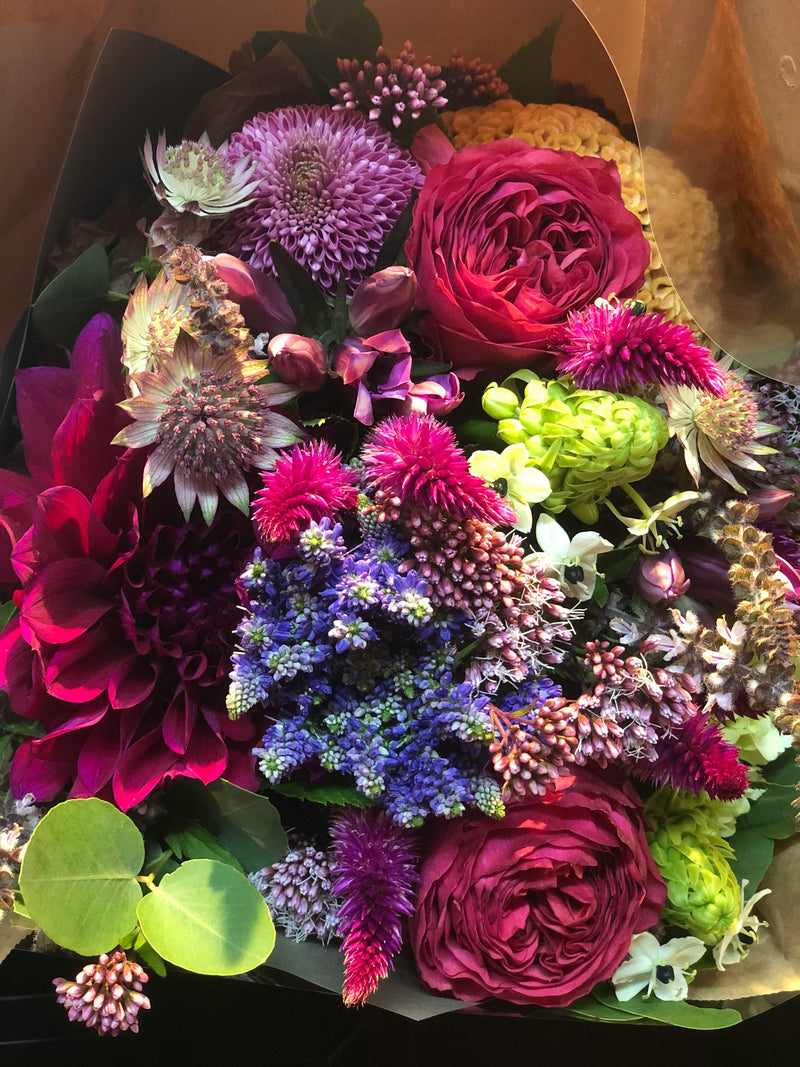 Jewel-toned bouquet of deep red roses, dahlias and celosia in kraft wrap